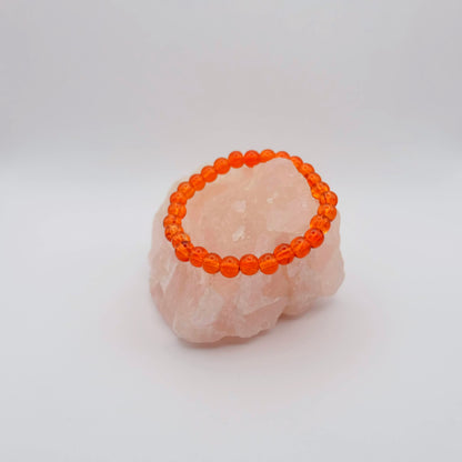 Orange beaded bracelet on a pink stone with a white background