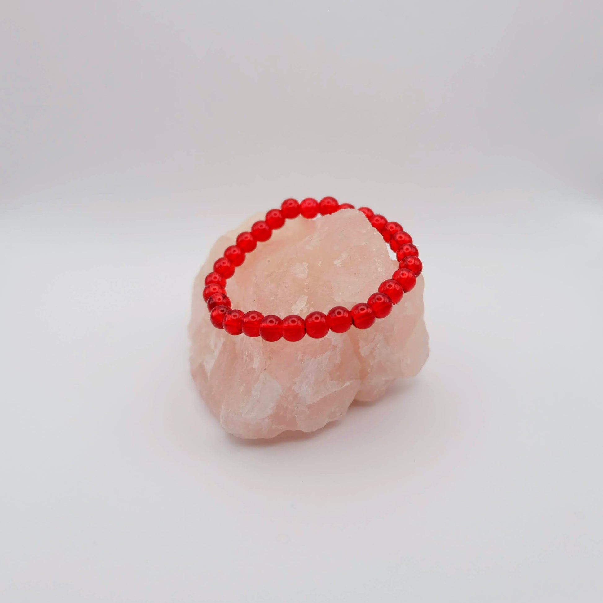 Red beaded bracelet on a pink stone with a white background