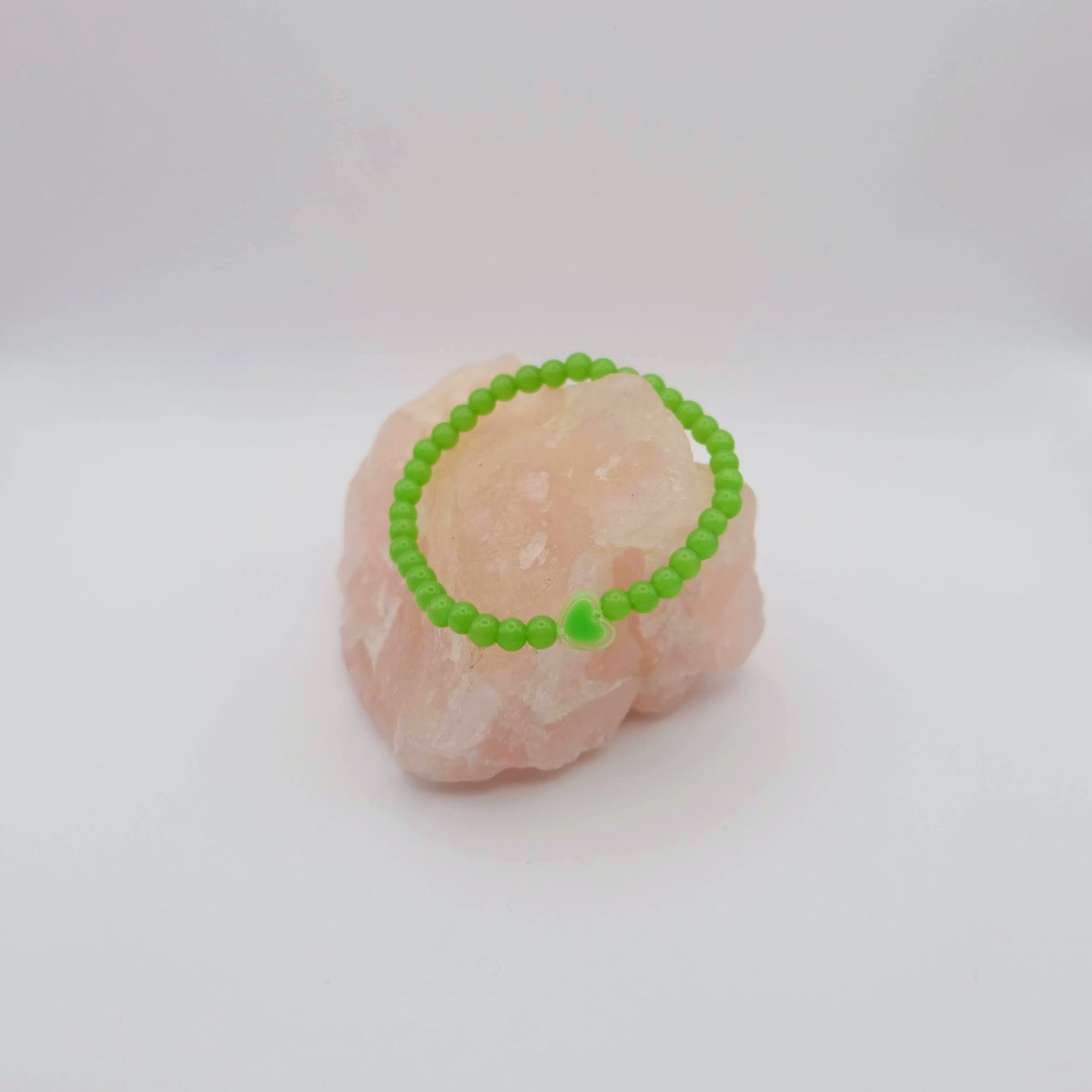 Green beaded bracelet on a pink stone against a white background