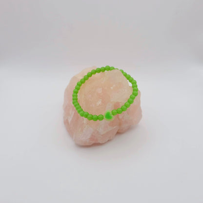 Green beaded bracelet on a pink stone against a white background