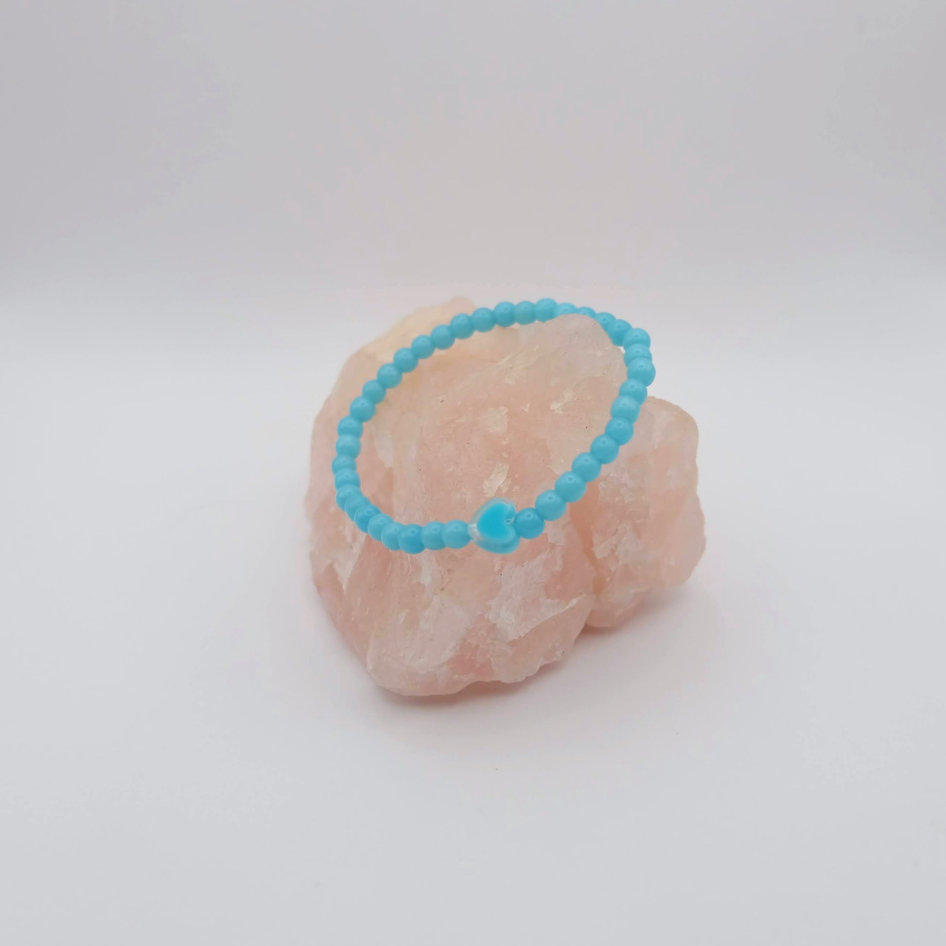 Blue/Turquoise beaded bracelet on a pink stone against a white background