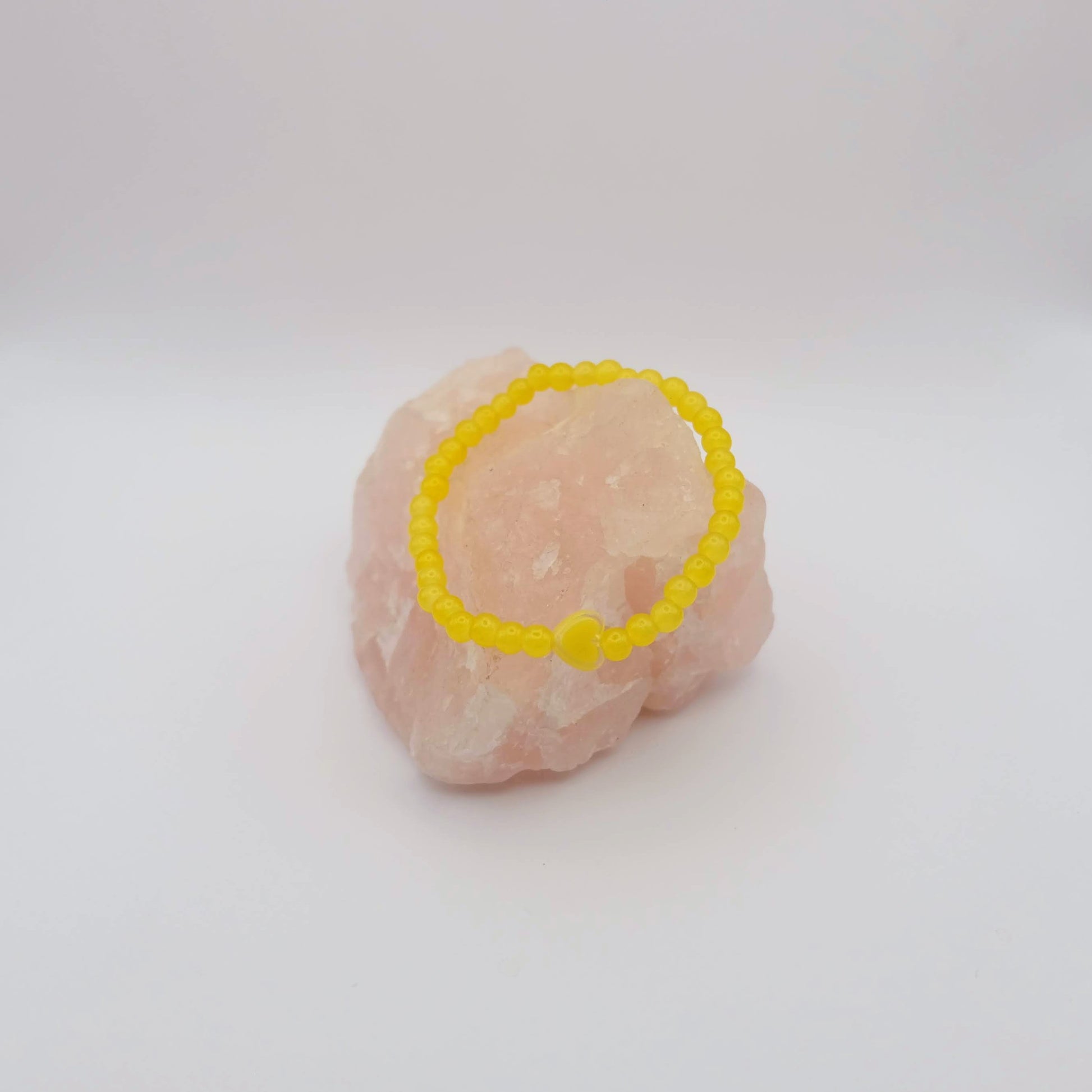 Yellow beaded bracelet on a pink stone against a white background