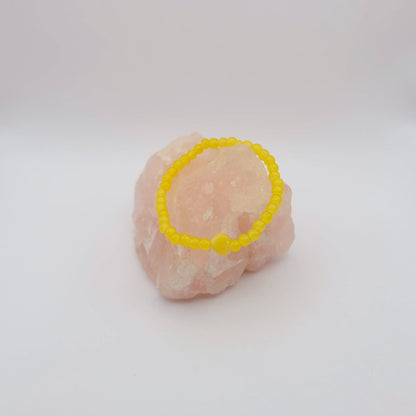 Yellow beaded bracelet on a pink stone against a white background