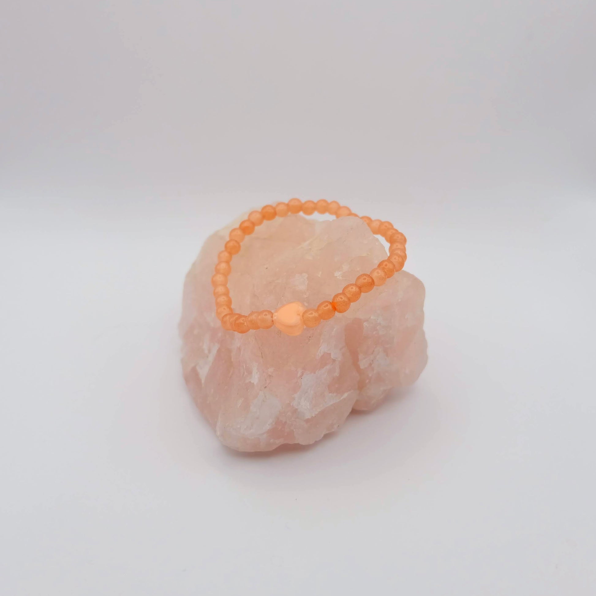 Orange beaded bracelet on a pink stone against a white background