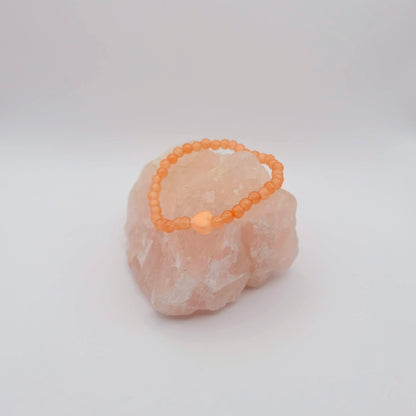 Orange beaded bracelet on a pink stone against a white background