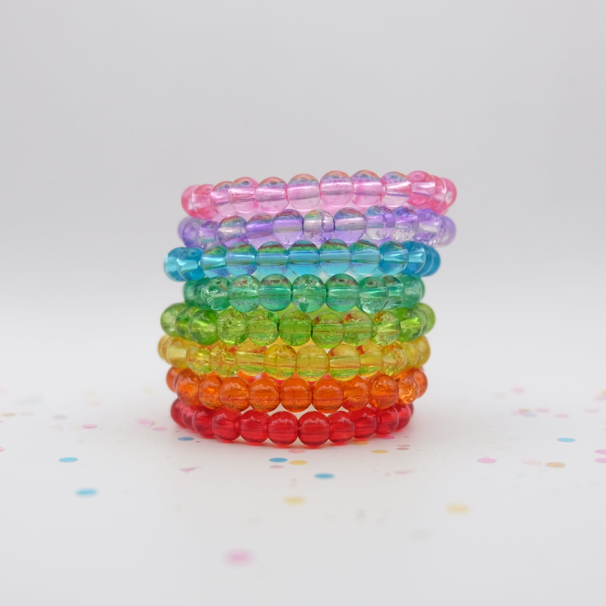 Stack of rainbow-colored beaded bracelets on a white background with colorful confetti.