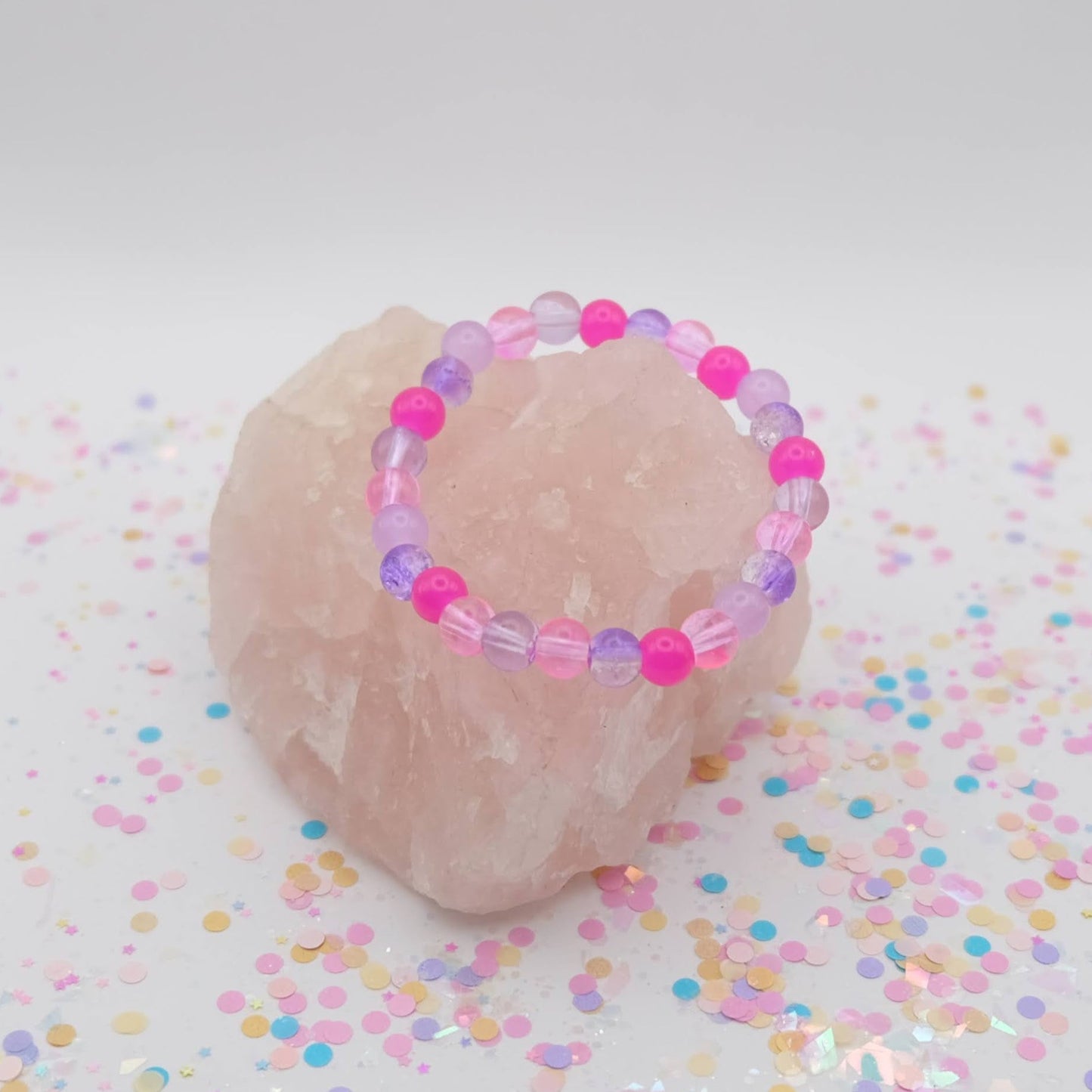 Pink and purple beaded bracelet on a pink stone with colorful confetti on a white background