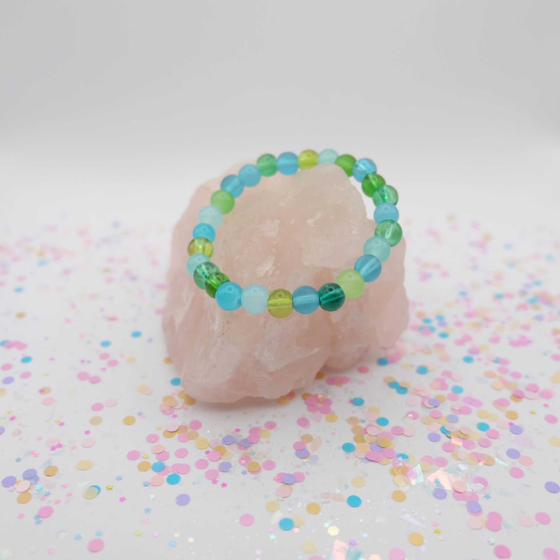 Green,  aqua and blue beaded bracelet on a pink stone with confetti background
