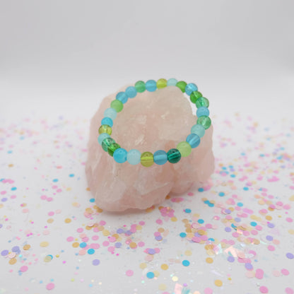 Green,  aqua and blue beaded bracelet on a pink stone with confetti background