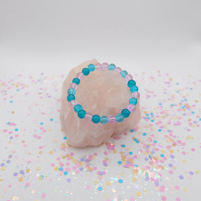 Turquoise and purple beaded bracelet on a pink stone with colorful confetti on a white background