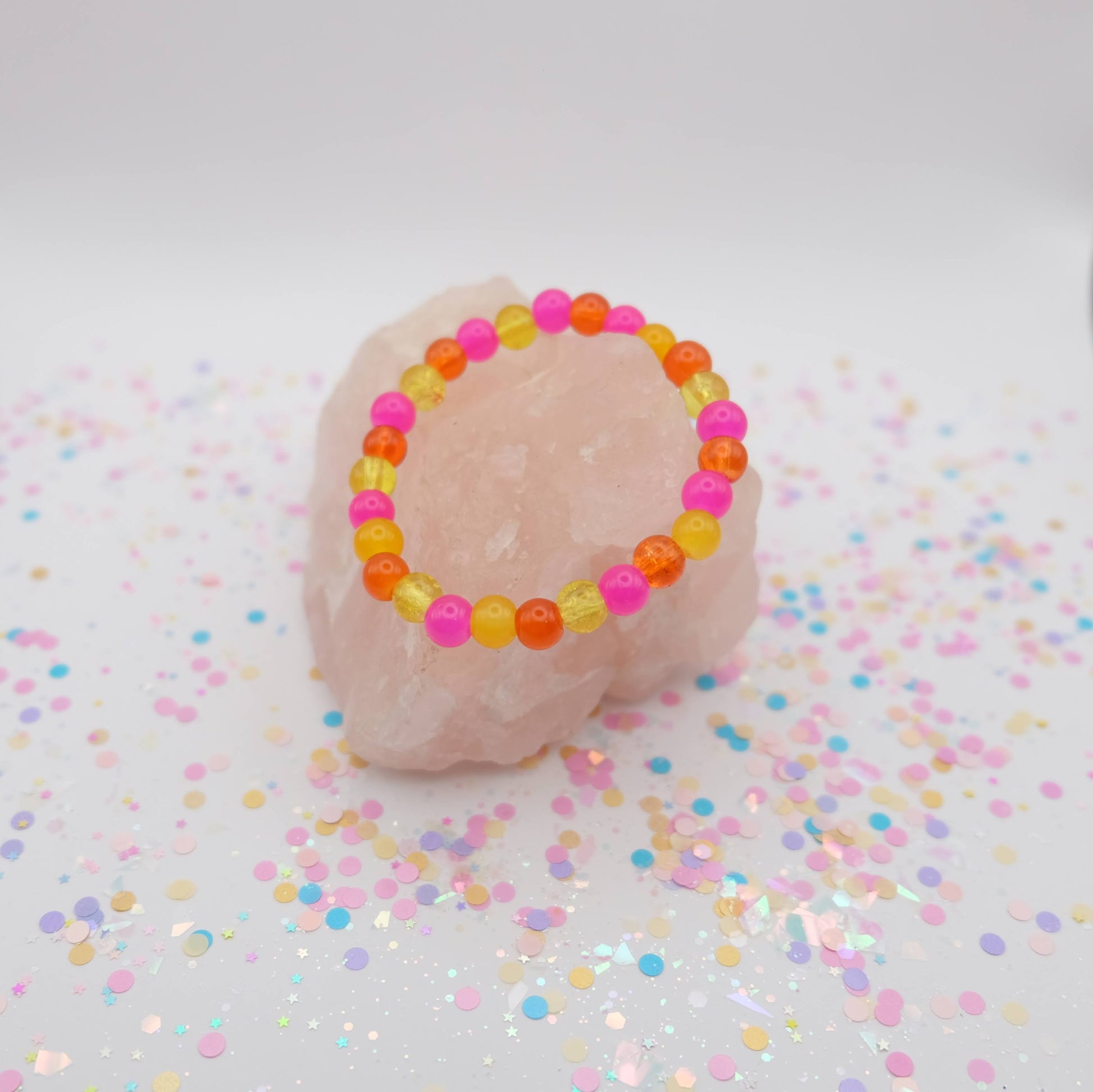 Pink, yellow and orange beaded bracelet on a pink rock with confetti background