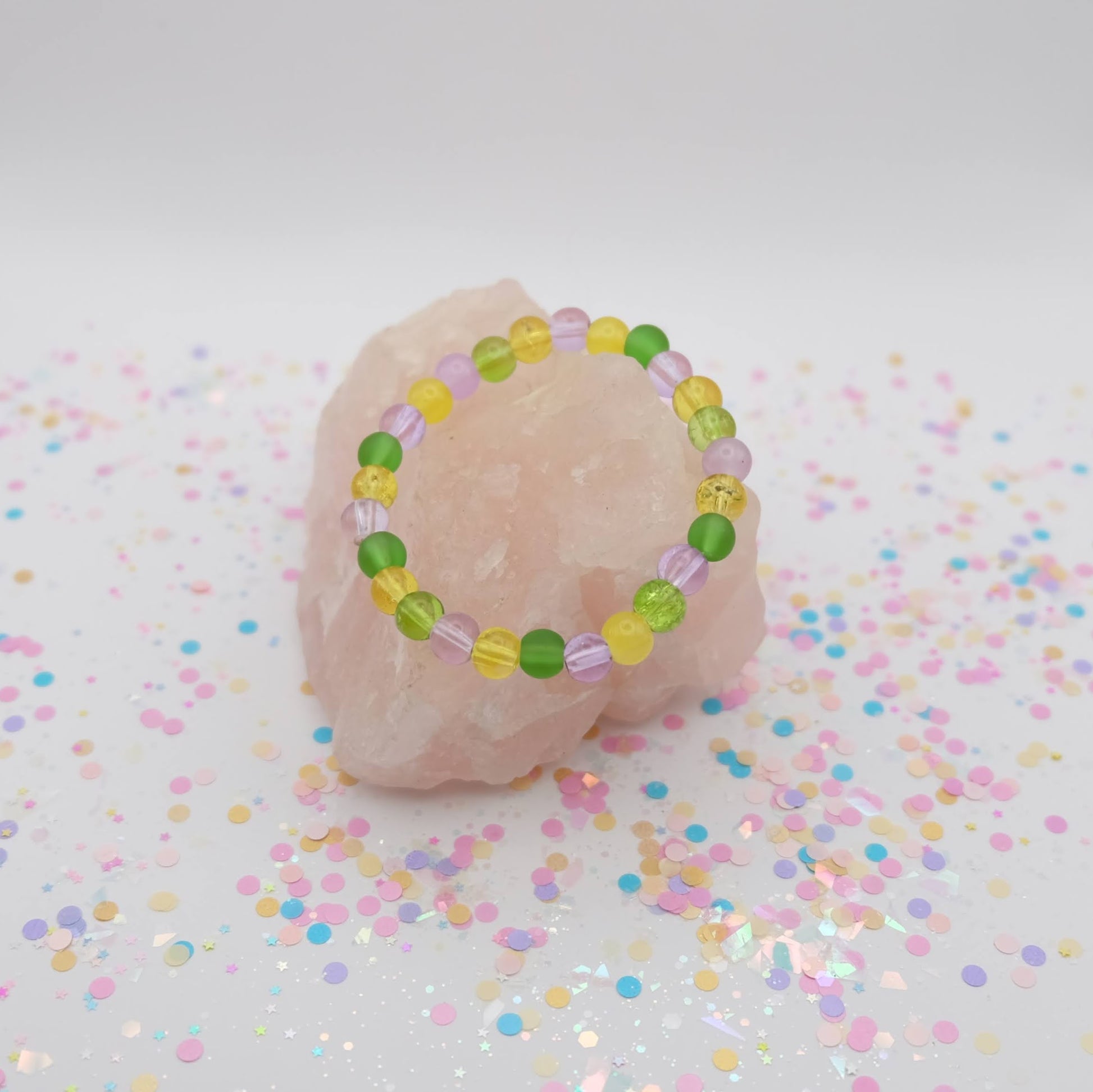 Green, purple and yellow beaded bracelet on a pink rock with a pastel confetti background