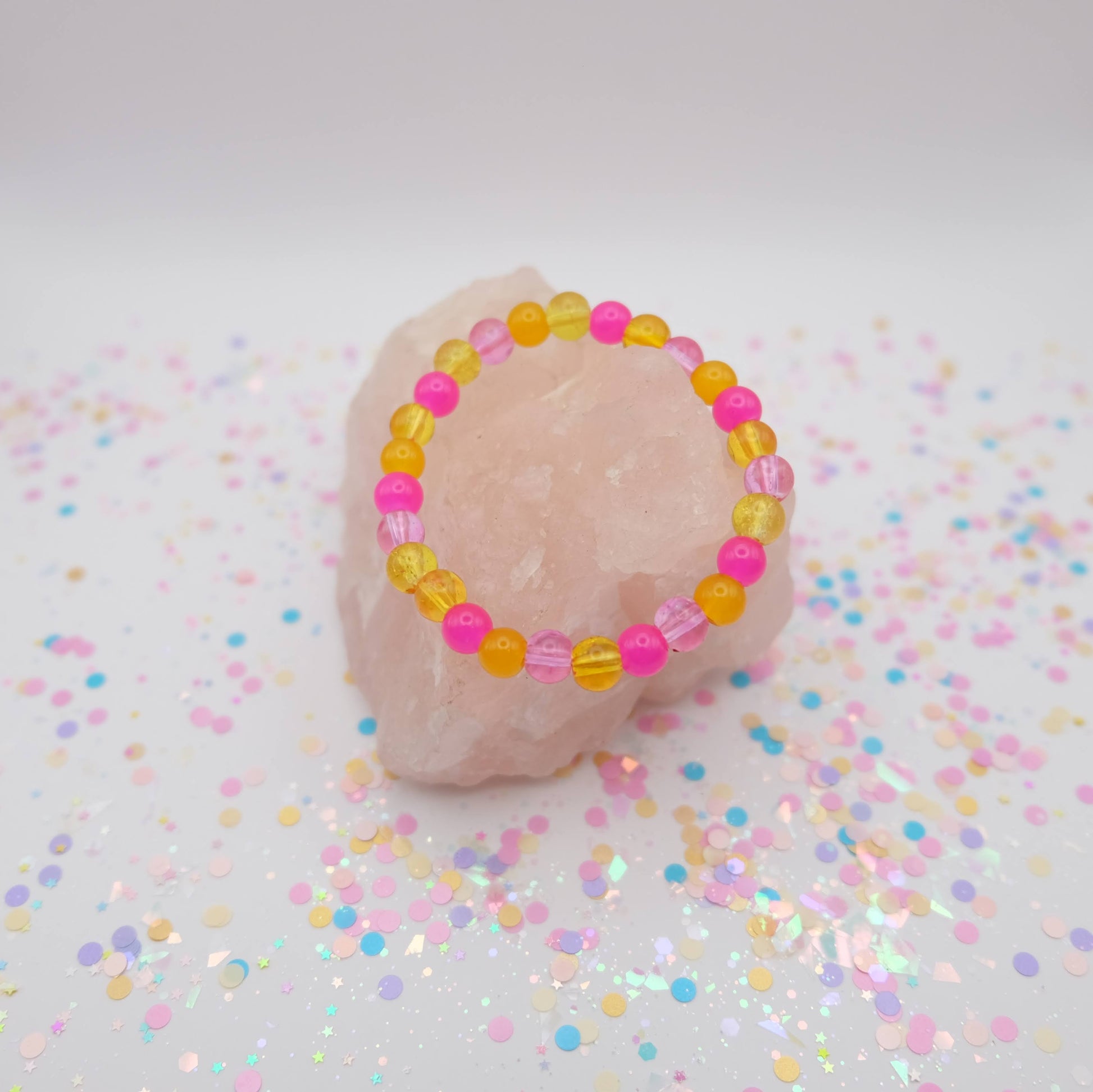 Pink and yellow beaded bracelet on a pink stone with confetti background