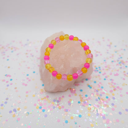 Pink and yellow beaded bracelet on a pink stone with confetti background