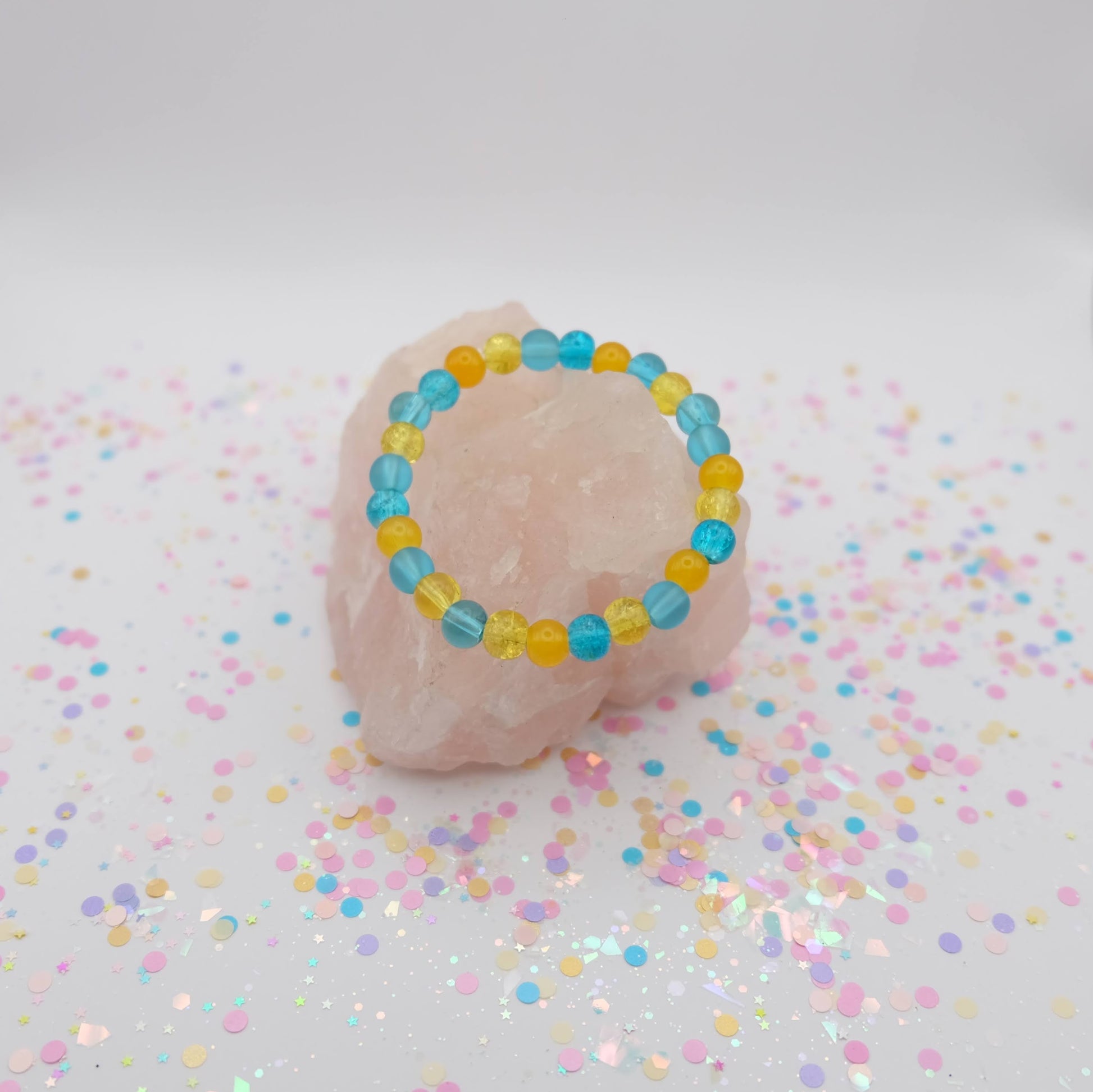Blue and yellow beaded bracelet on a pink stone with confetti on a light background