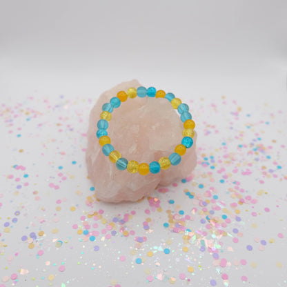 Blue and yellow beaded bracelet on a pink stone with confetti on a light background