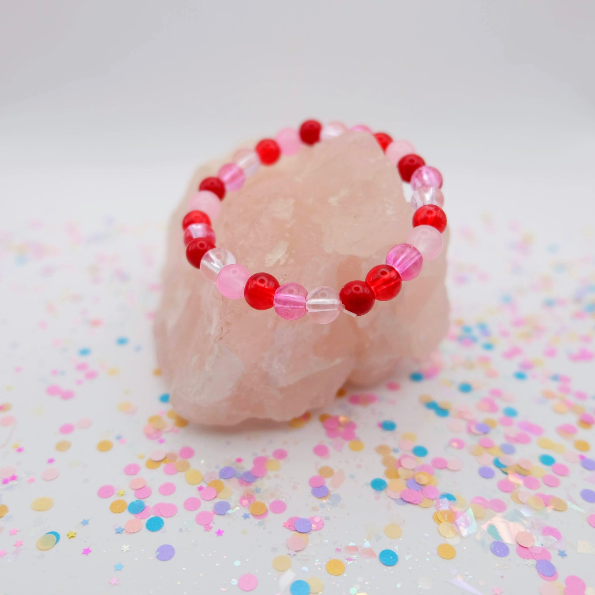 Beaded bracelet with red and pink beads on a white stone with colorful confetti
