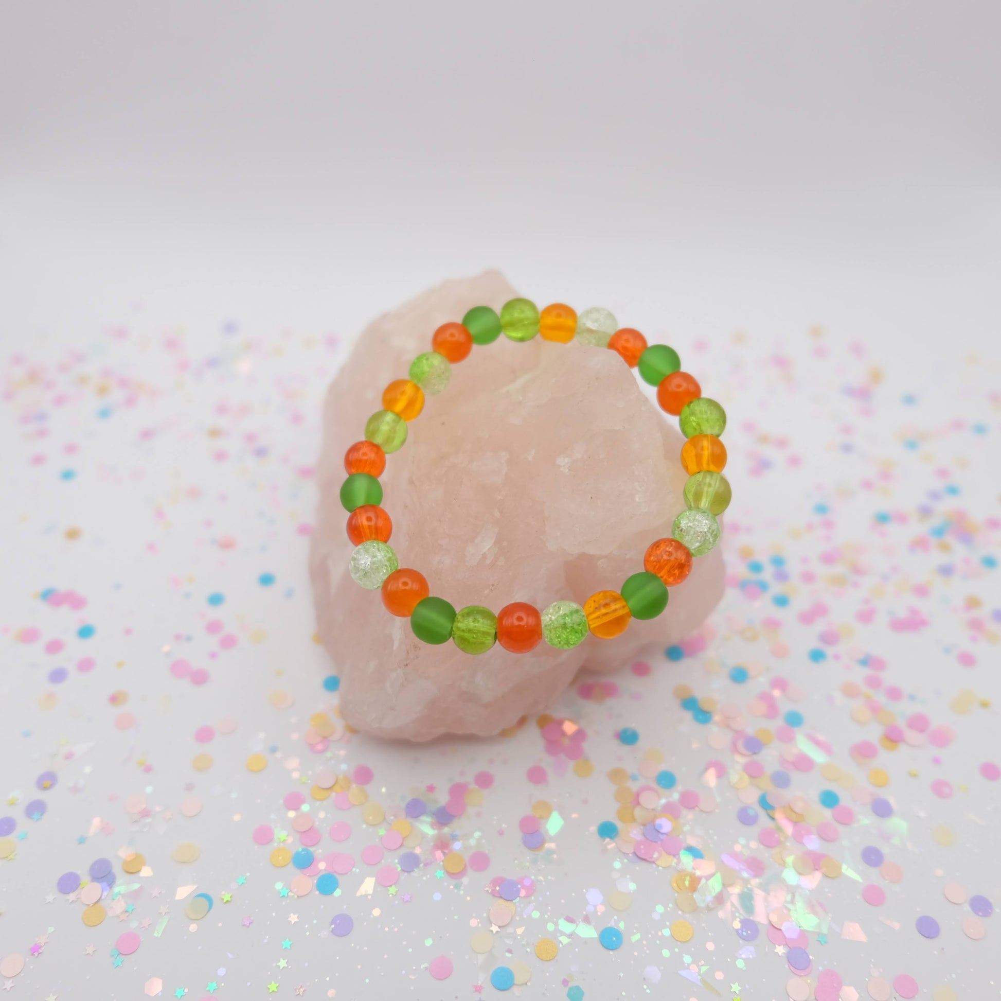 Green and orange beaded bracelet on a pink object with confetti background