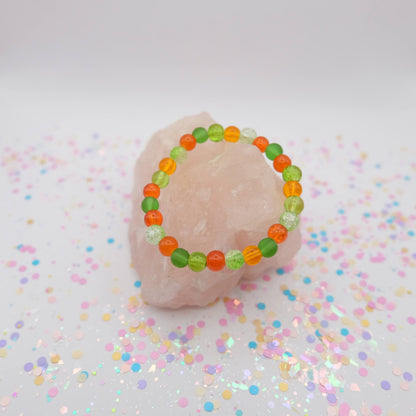 Green and orange beaded bracelet on a pink object with confetti background