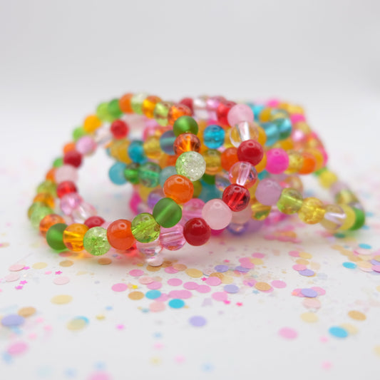 Colorful beaded bracelets on a white surface with confetti