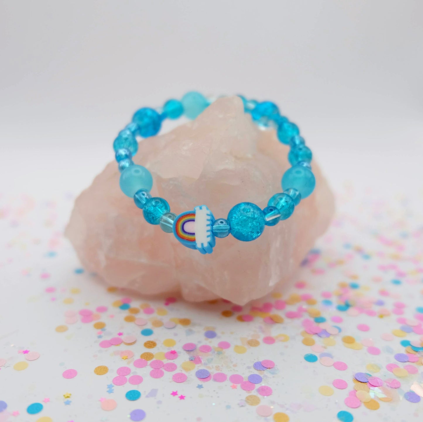 Blue beaded bracelet with a polymer clay rainbow bead on a pink stone with colorful confetti