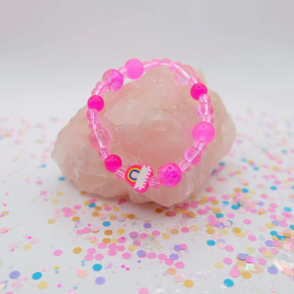Pink beaded bracelet with a polymer clay rainbow bead on a pink stone with colorful confetti