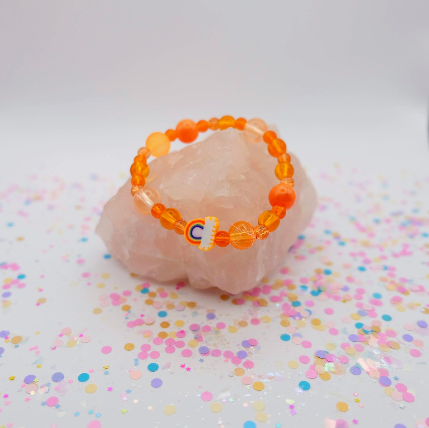 Orange beaded bracelet with a polymer clay rainbow bead on a pink stone with colorful confetti
