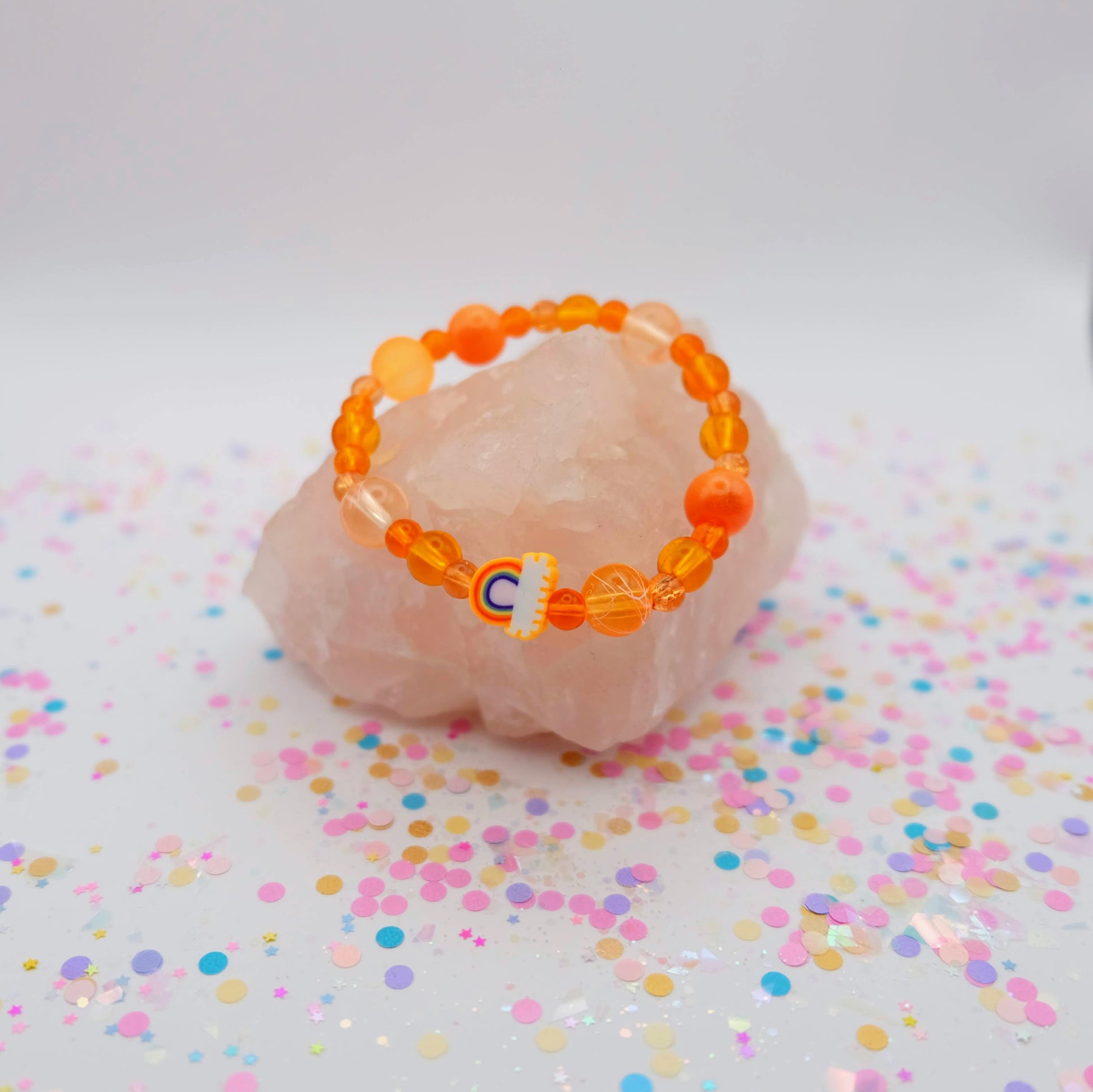 Orange beaded bracelet with a polymer clay rainbow bead on a pink stone with colorful confetti