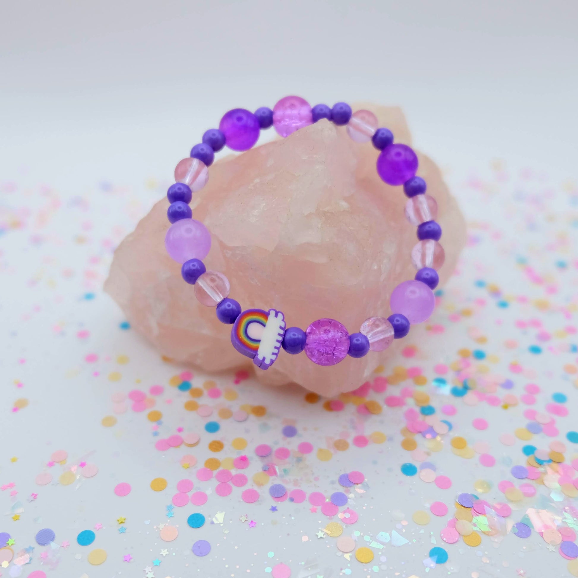 Purple beaded bracelet with a polymer clay rainbow bead on a pink stone with colorful confetti