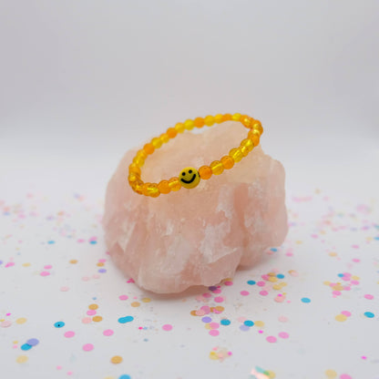 Yellow beaded bracelet with a smiley face charm on a pink stone with colorful confetti