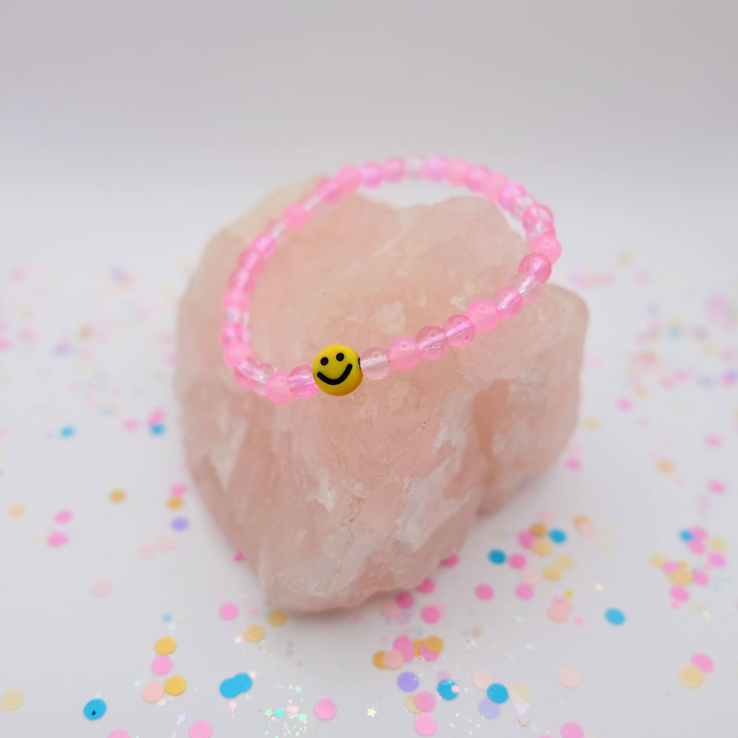 Pink beaded bracelet with a smiley face charm on a pink stone with colorful confetti
