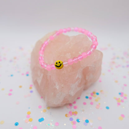 Pink beaded bracelet with a smiley face charm on a pink stone with colorful confetti