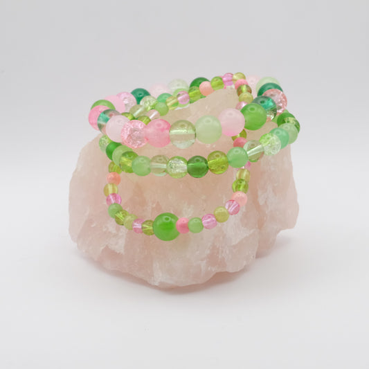 Set of green and pink beaded bracelets on a pink stone with a white background