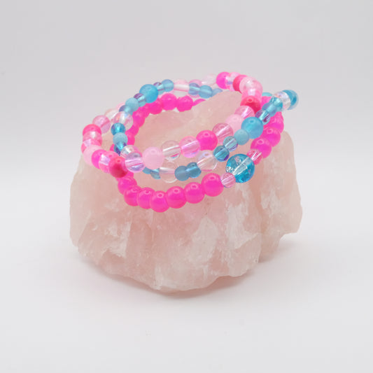 Stack of pink and blue beaded bracelets on a rose quartz stone against a white background