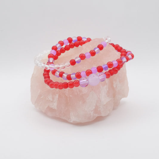 Three  red and purple elastic beaded bracelets on a pink crystal with a white background
