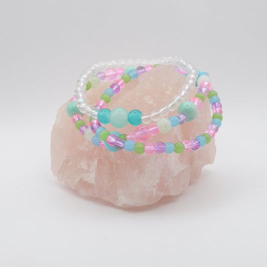 Set of colorful elastic beaded bracelets in pink, purple, green,  blue and white on a rose quartz stone with a white background
