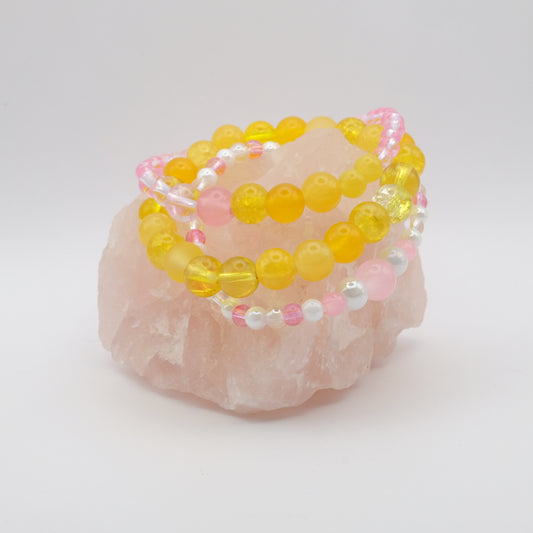 Yellow and pink beaded bracelets on a rose quartz stone with a white background