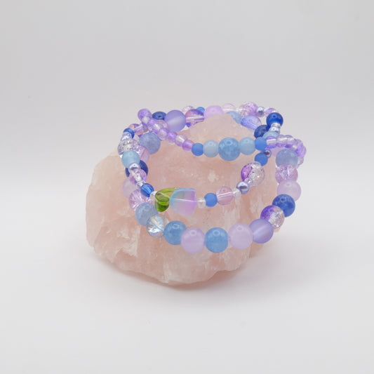 Set of navy, blue and purple elastic beaded bracelets with a glass flower bead on a pink stone with a white background