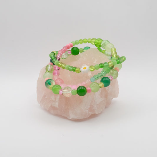 A stack of pink and green elastic beaded bracelets with a single daisy bead on a pink  quartz rock.