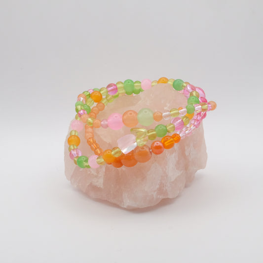 A stack of bracelets in pink, orange and green with a single glass flower bead.
