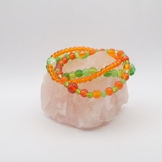 A stack of bracelets in orange and green on a rose quartz.