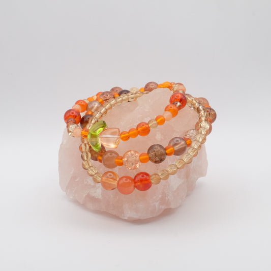 A stack of elastic beaded bracelets in beautiful autumn tones  or orange ad brown with pops of bronze and a single orange glass flower bead