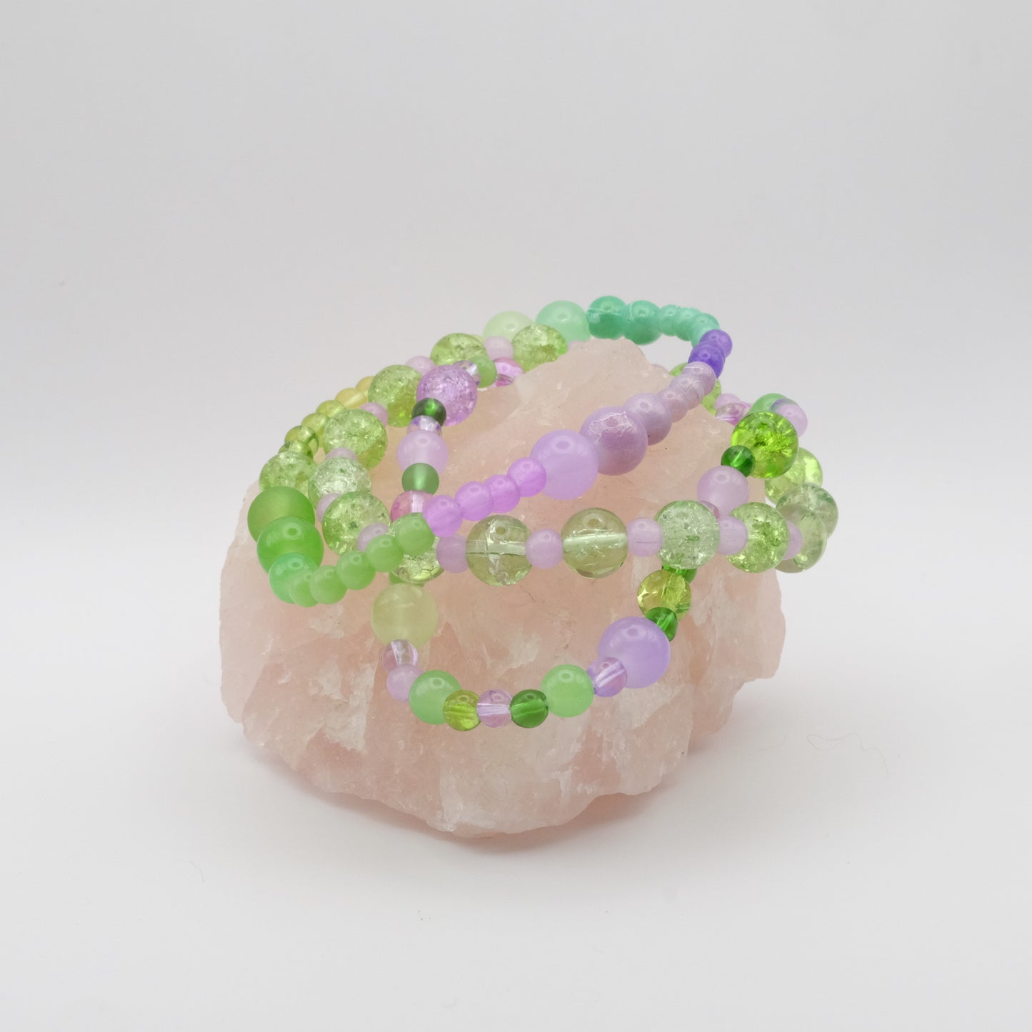 Beaded bracelets with green and purple beads on a pink stone against a white background