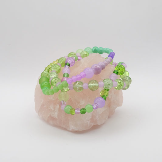 Beaded bracelets with green and purple beads on a pink stone against a white background