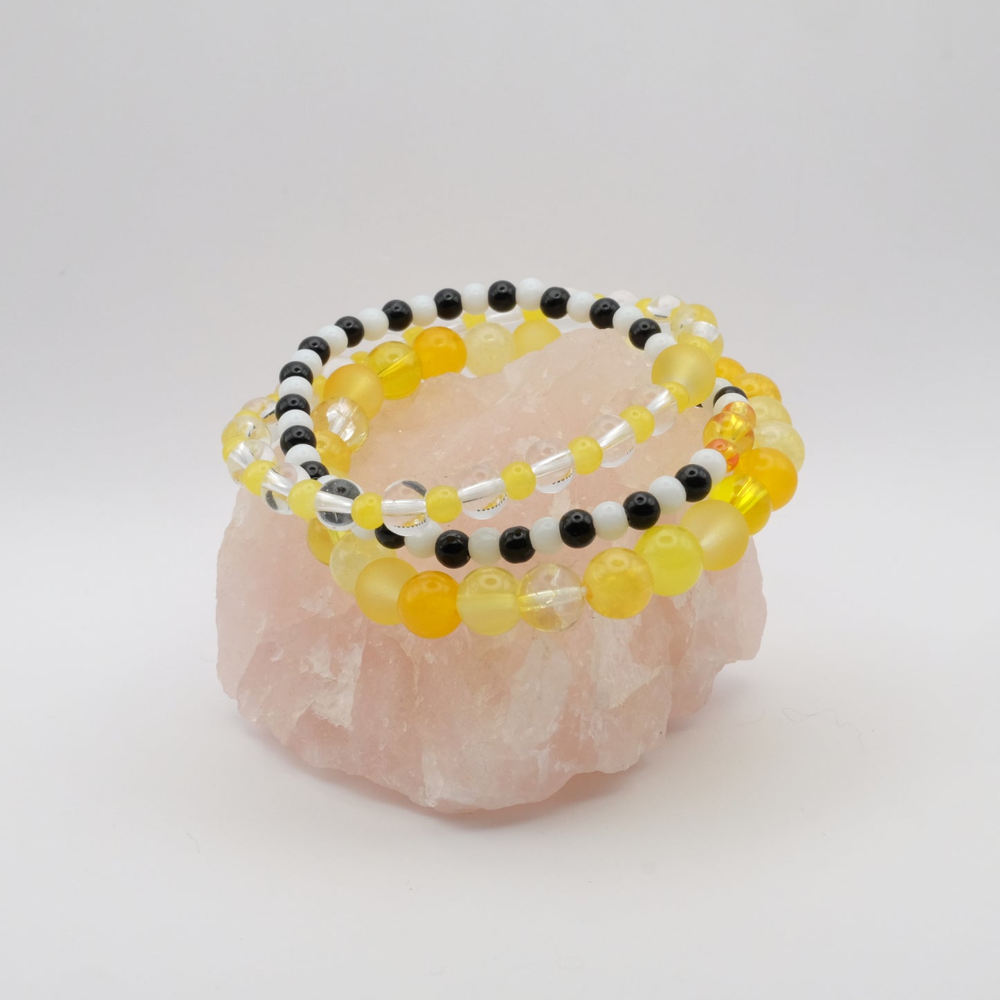 A stack of elastic beaded bracelets in yellow, black and white on a rose quartz rock