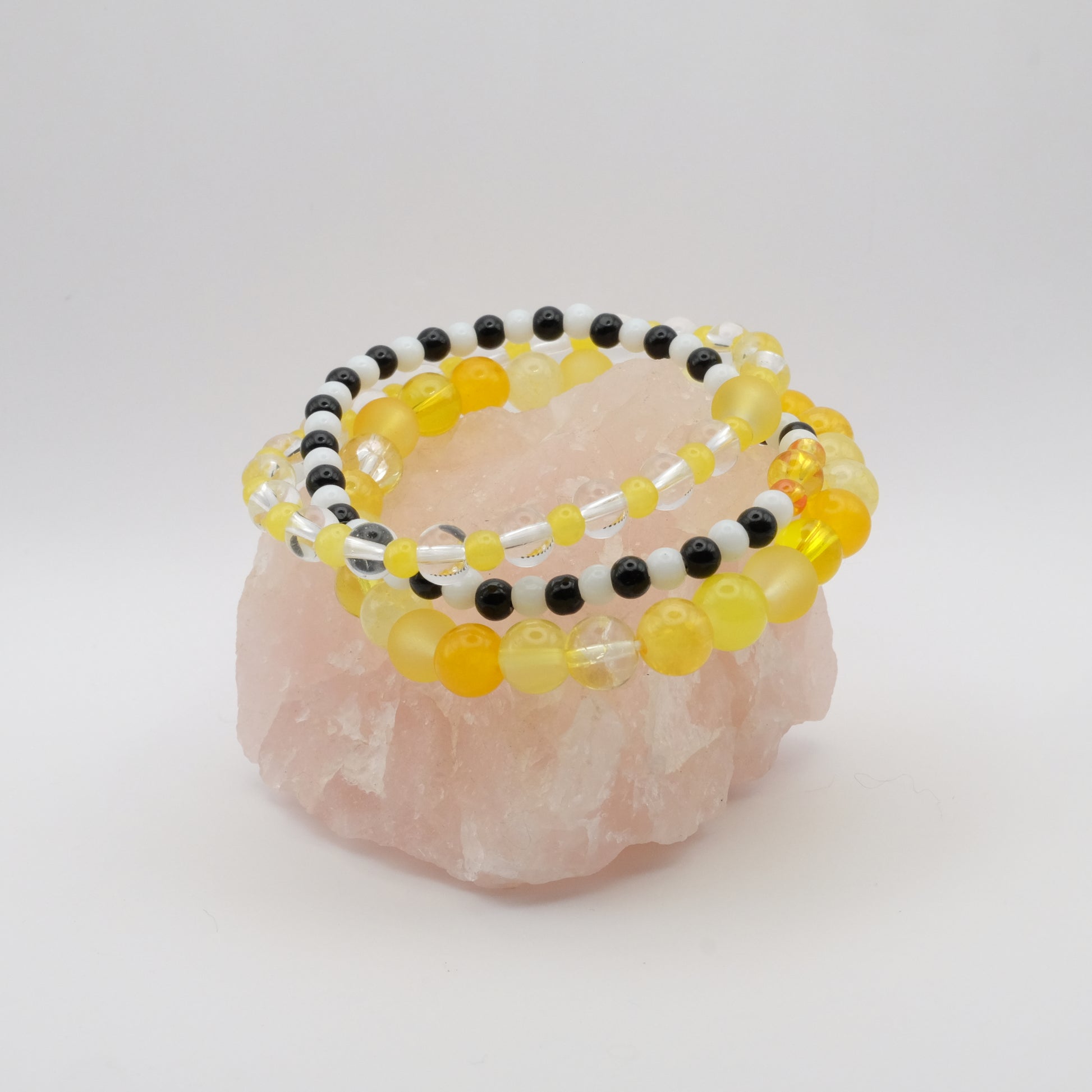 A stack of elastic beaded bracelets in yellow, black and white on a rose quartz rock