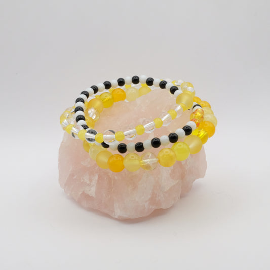 A stack of elastic beaded bracelets in yellow, black and white on a rose quartz rock