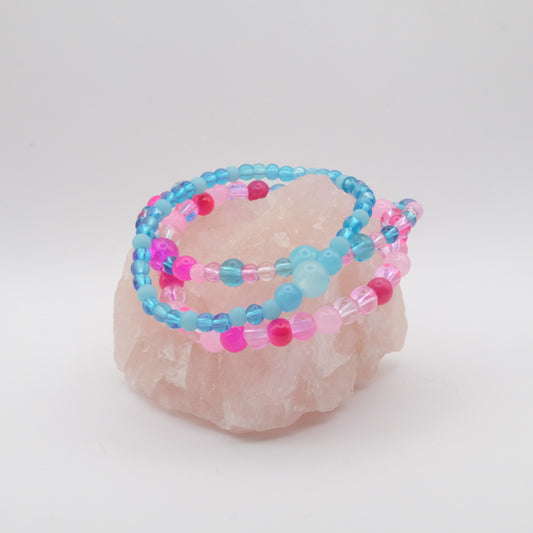 A stack of elastic beaded bracelets in pink and blue on a rose quartz rock