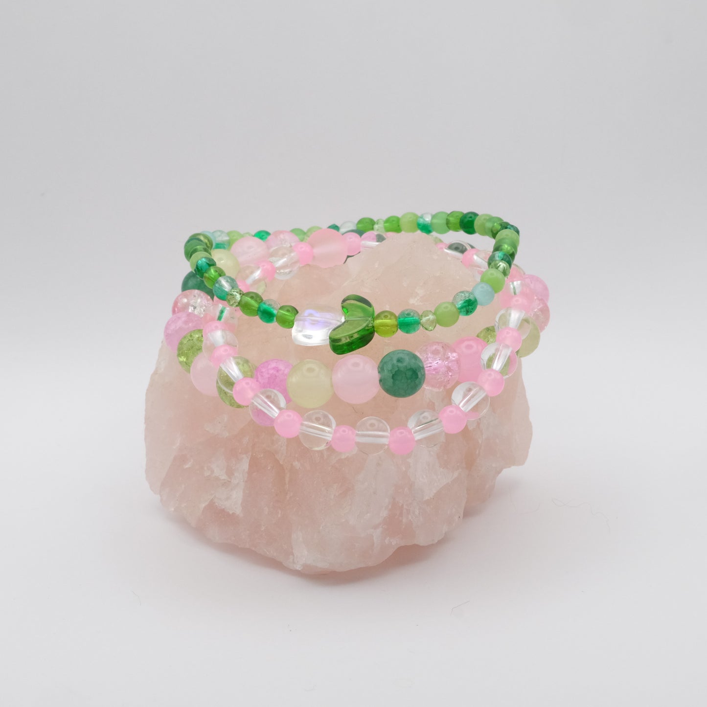 A stack of elastic beaded bracelets in pink and green with a single clear glass flower bead on a rose quartz rock