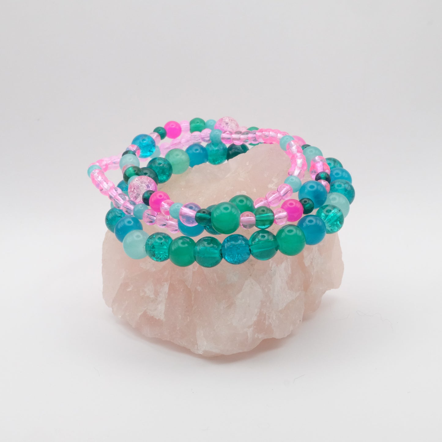 Stack of teal, aqua and pink beaded bracelets on a white background